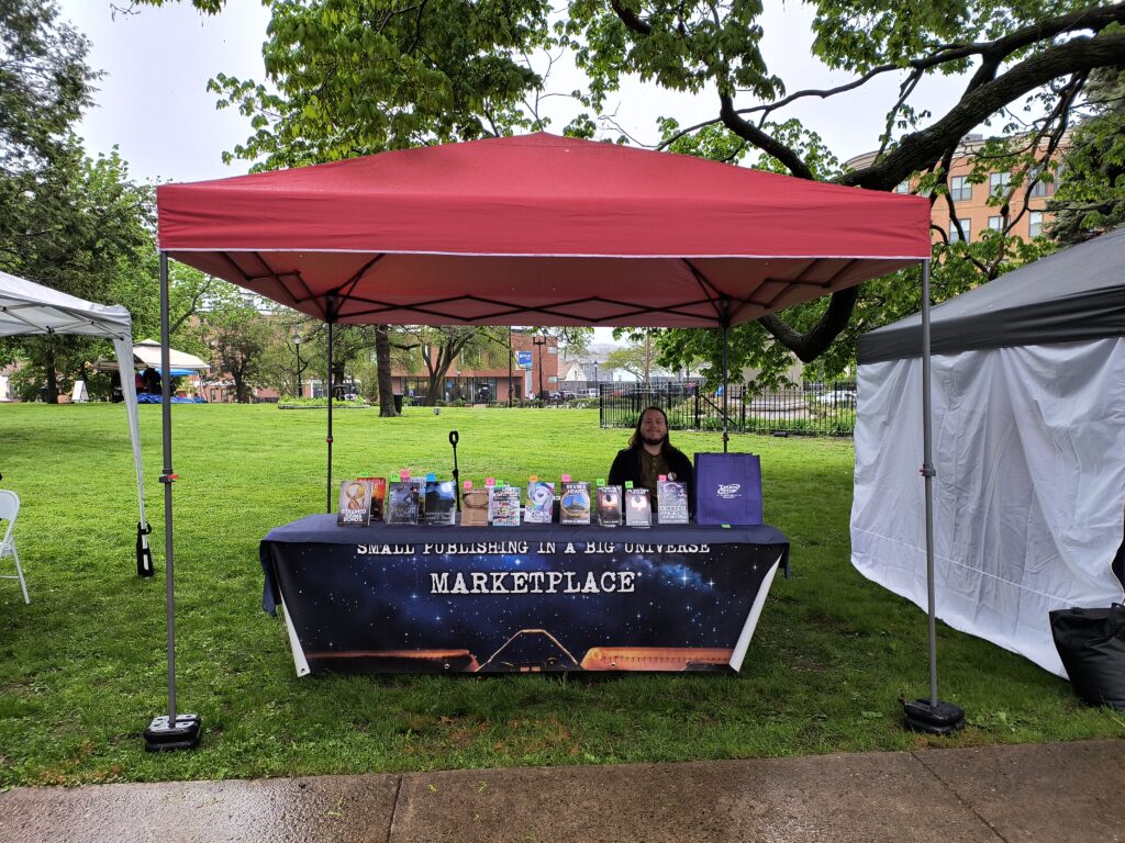 a booth with a red canopy with a limited selection of books in the rain