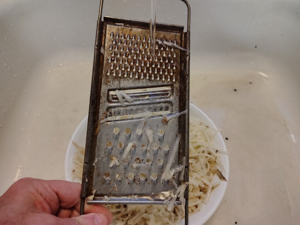 Rinsing the grater and filling the bowl of grated potatoes with water.