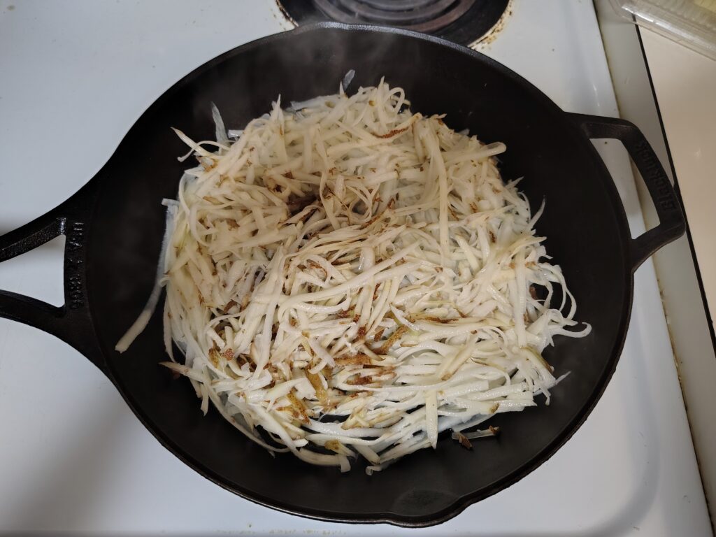Grated potatoes spread out in a cast iron skillet.