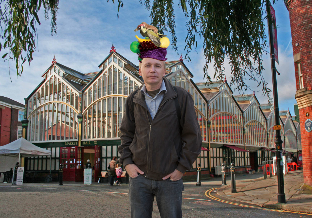 an image of Källë Kniivilä, Tutmonda Ĵurnalisto, photoshopped in front of some building — in England, if I recall correctly — wearing a Carmen Miranda hat with a weasel riding a woodpecker on top.